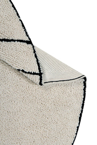 Detail van Trace-vloerkleed met zwarte lijnen, omgeslagen rand en achterzijde.