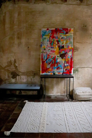 Naturel Tribu-vloerkleed met verhoogde geometrische motieven en kwastjes bij een kunstwerk.