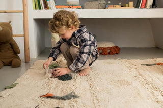 Kind speelt met groentefiguren op een naturel vloerkleed.