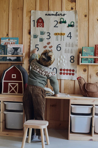 Kind bij een wandhanger met cijfers en boerderijfiguren.