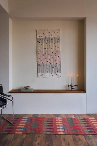 Siennarode Intersecting-loper met veelkleurige blokken langs een wandnis.