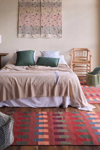 Siennarode Intersecting-vloerkleed met blokmotieven naast een bed.