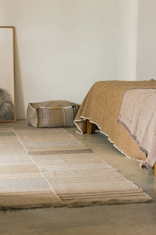 Puebla-poef met strepen naast een bed.