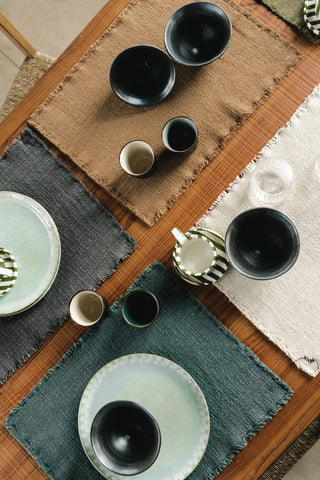 Handloom-placemat in donkergroen met korte franjerand met servies op een gedekte tafel.