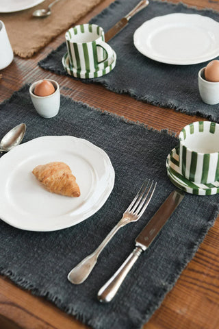 Handloom-placemat in donkergrijs met korte franjerand met servies op een gedekte tafel.