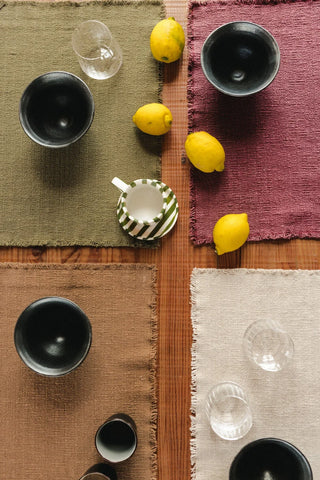 Handloom-placemat in marsala met korte franjerand met servies op een gedekte tafel.