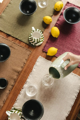 Handloom-placemat in naturel met korte franjerand met servies op een gedekte tafel.