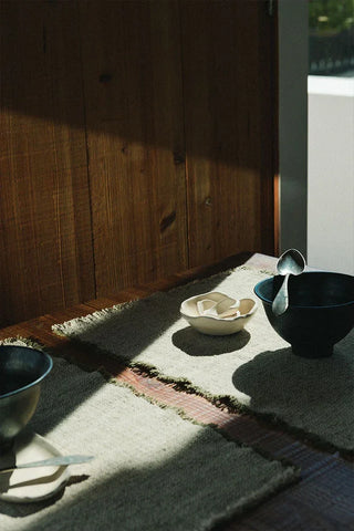 Handloom-placemat in naturel met kaki rand met servies op een tafel.