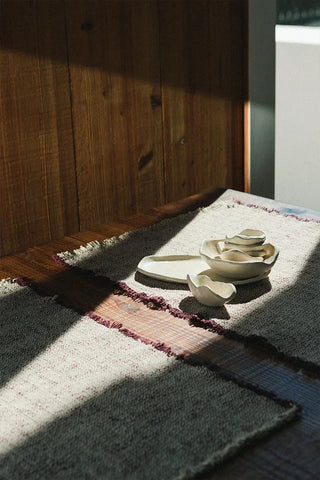 Handloom-placemat in naturel met marsalarand met servies op een tafel.