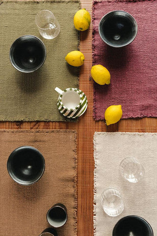 Handloom-placemat in oker met korte franjerand met servies op een gedekte tafel.