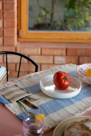 Blauwe placemat met bestekvak en een bord op tafel.
