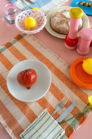 Oranje gestreepte placemat met bestekvak op een gedekte tafel.