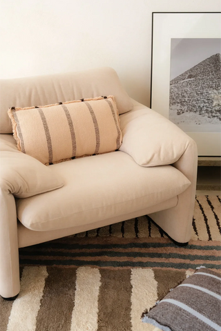 Lichtroze gestreept kussen op een lichte fauteuil.