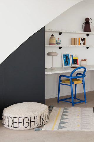 Naturel ABC-poef met zwarte letters bij een bureau en blauwe stoel.