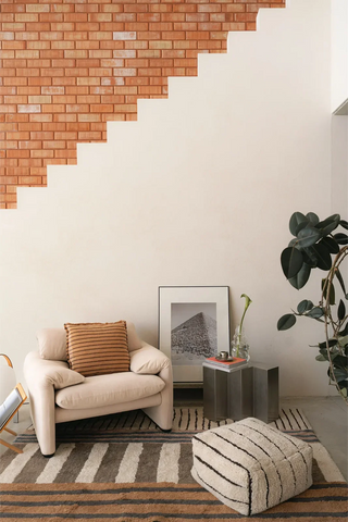 Lichte gestreepte Lines-poef bij een fauteuil.