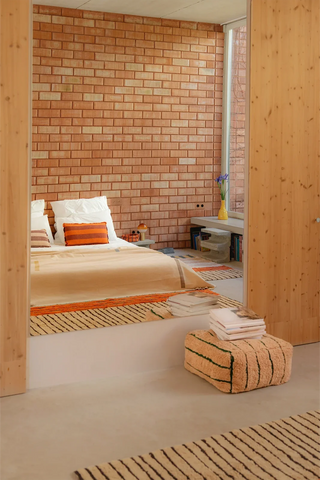 Roze Lines-poef naast een bed in een lichte slaapkamer.