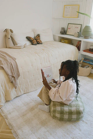 Kind leest op een groene geruite Vichy-poef naast een bed.