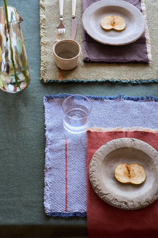 Vertical-placemat in blauw met bord en bestek op een gedekte tafel.