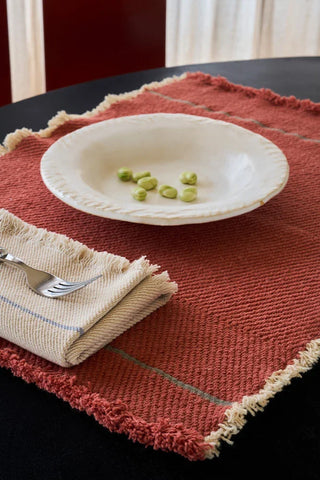 Vertical-placemat in terracottarood met bord en bestek op een gedekte tafel.