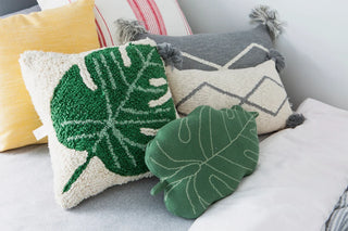 Kussen met groen monsterablad bij andere kussens op een bed.