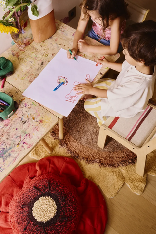 Rood bloemkussen naast een tekentafel in een kinderkamer.