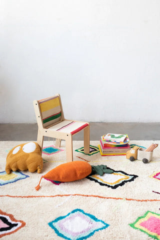 Kaarol-stoelhoes met gekleurde strepen op een houten kinderstoel tussen speelgoed.