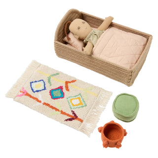 Mini Lorena Nari met pop in mandbed, naturel beddengoed en kleurrijk kleedje.