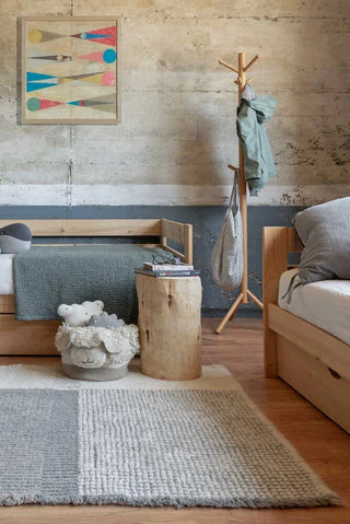 Kaia Smoke Blue-vloerkleed met blauwgrijze vakken in een kamer met bank en kapstok.