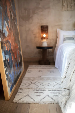 Naturel Lakoda-vloerkleed met geometrische motieven bij een bed.