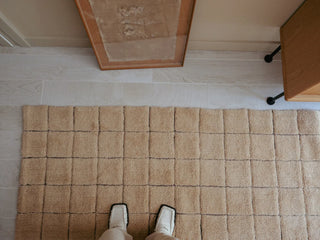 Detail van amberkleurig Mosaic-vloerkleed met rasterpatroon op de vloer.