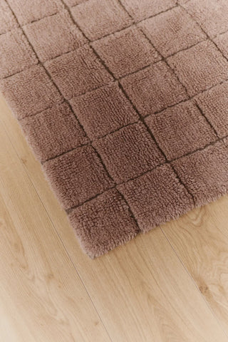 Hoekdetail van roze Mosaic-vloerkleed op een houten vloer.