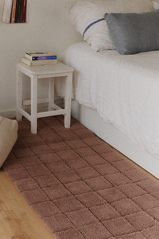 Roze Mosaic-vloerkleed naast een bed.