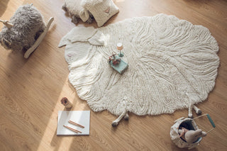 Pink Nose Sheep-vloerkleed met golvende poolstructuur en speelgoed op een houten vloer.