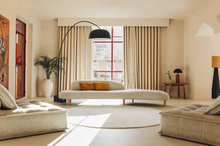 Rond licht vloerkleed voor een bank en lage fauteuils in een woonkamer.