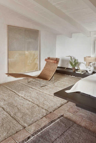 Beige Steppe-vloerkleed bij een ligstoel en bed, met een donker kleed op de voorgrond.