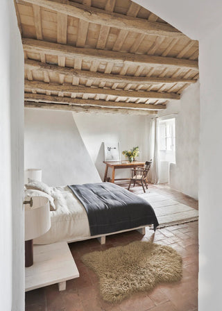 Beige Woolly-vloerkleed met organische contour naast een bed.