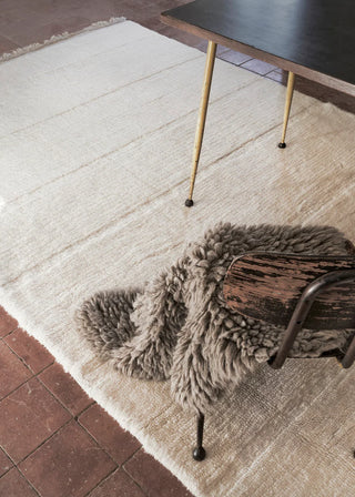 Grijs Woolly-vloerkleed over een houten stoel bij een tafel.