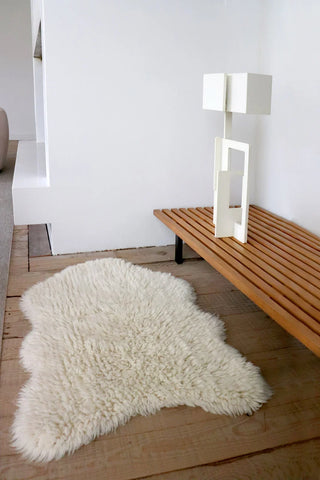 Wit Woolly-vloerkleed met organische contour bij een houten bankje.
