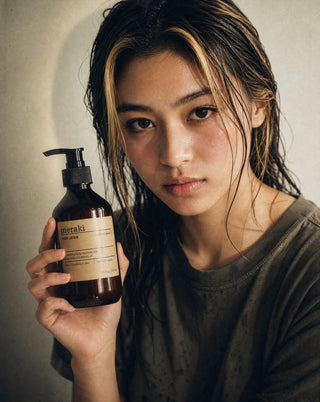 Vrouw houdt de Meraki Northern Dawn bodylotion in pompflacon naast haar gezicht