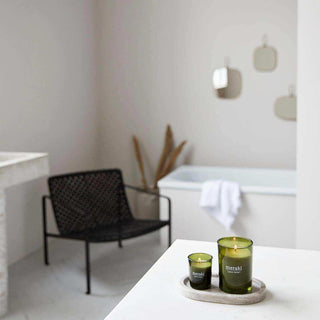 Twee Meraki Green Herbal geurkaarsen op een rond dienblad in een badkamer