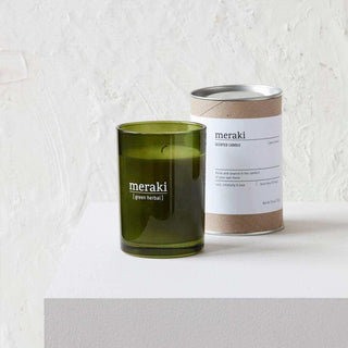 Meraki Green Herbal geurkaars in groen glas naast de verpakking op witte sokkel