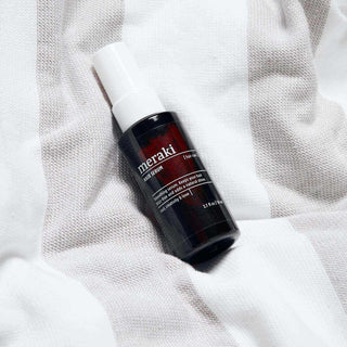 Meraki Hair Serum liggend op licht geweven textiel, met pompflacon en zichtbaar etiket