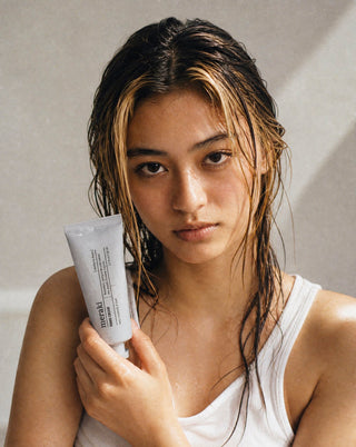 Model houdt de witte tube Meraki Hand Cream Northern Dawn naast haar gezicht