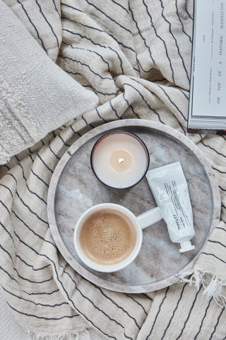 Meraki handcrème op een dienblad met een kop koffie, brandende kaars en gestreepte handdoek