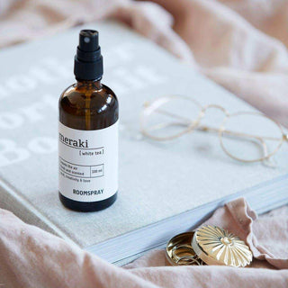 Meraki roomspray White Tea op een boek naast bril en sieraden