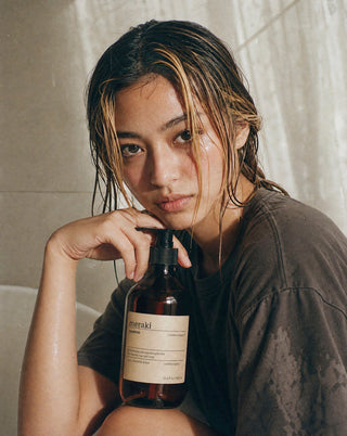 Persoon met nat haar houdt een Meraki Northern Dawn shampoo met pomp vast