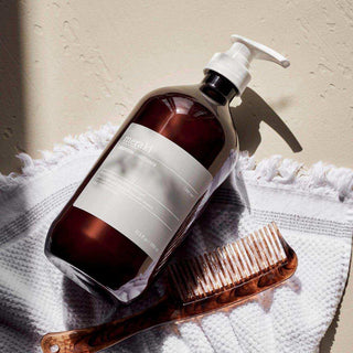 Meraki volumising conditioner in pompflacon naast een bruine kam op een witte handdoek