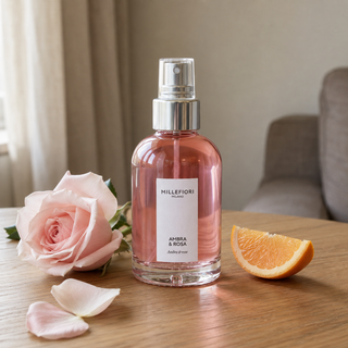 Millefiori Milano Home Spray 100 ml Ambra & Rosa op een houten tafel, met een roos en sinaasappel als verwijzing naar de geur.