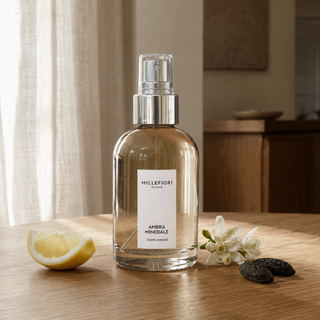 Millefiori Milano Home Spray 100 ml Ambra Minerale op een houten tafel met citrus, witte bloemen en tonkabonen in zacht raamlicht.