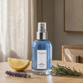 Millefiori Milano Home Spray 100 ml Blue Posidonia op een houten tafel met citroen, lavendel en rozemarijn in zacht raamlicht.